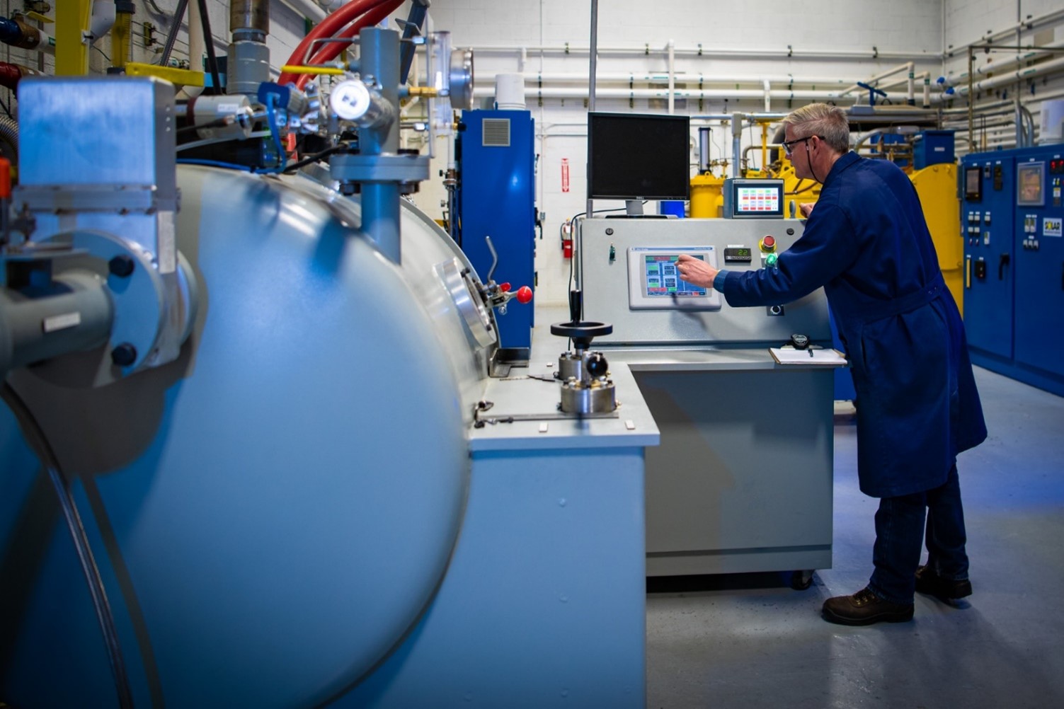 A male scientist in a blue lab coat standing at an computer inside of the Center for Sustainable Fuels and Chemicals.