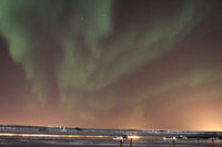 Aurora borealis over Kuparuk River Unit flowlines; glow on horizon from drillsites and Kuparuk Operations Center