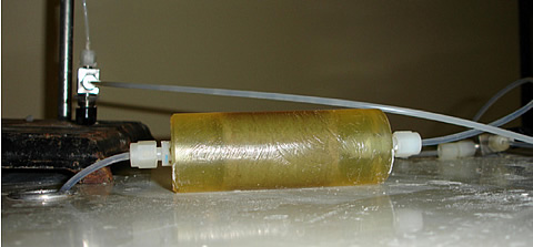 Epoxy-confined core in conjunction with temperature-controlled oven allows in-line analysis of nutrient uptake by microbes in the core. Note that the core is outside the oven. The microbes thrive at room temperature but not at elevated temperature, so all pumps, vessels, and flow lines are kept inside the oven to prevent reaction anywhere except inside the core.