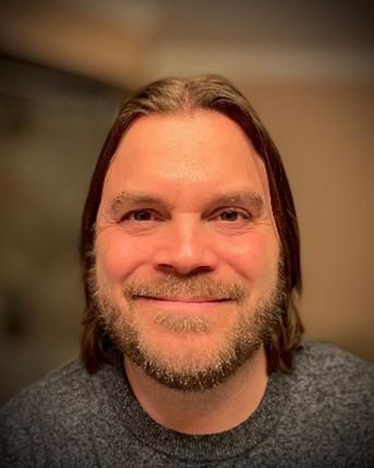 A photographer of Neil Kirschner, a  Caucasian man with shoulder length brown hair and a mustache and stubble with the same color.