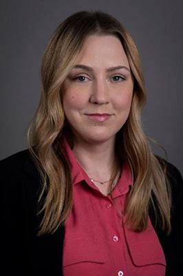 A portrait photograph of Krista Hill, a Caucasian woman with shoulder length dark blonde hair, blue eyes, a hot pink blouse and a black blazer.
