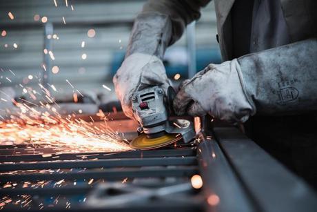 A person using a handheld angle grinder and sparks flying out from under the grinder. 