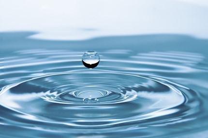 A close up shot of a water droplet hitting a pool of water.