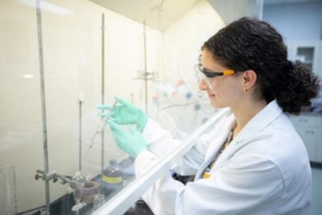 A Caucasian woman in a white lab coat filling a test tube by using a syringe.