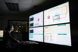 A man in a dark room looking a four brightly computer screens.