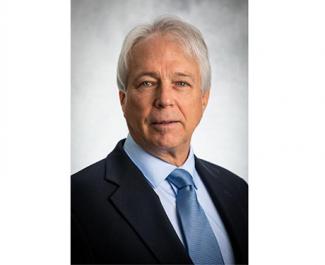 A headshot of Richard Dennis, A Caucasian man with grey hair, a black suit jacket and a light blue shirt and matching tie.